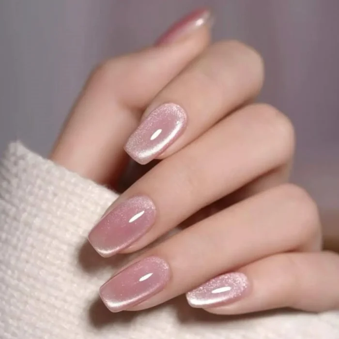 A hand with a sheer, velvety pink cat eye manicure on squoval nails, held against a white sweater sleeve.