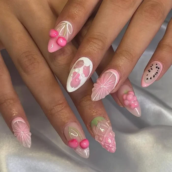 A set of long, stiletto nails with a monochrome pink 3D fruit design, including sculptural cherries and citrus slices.