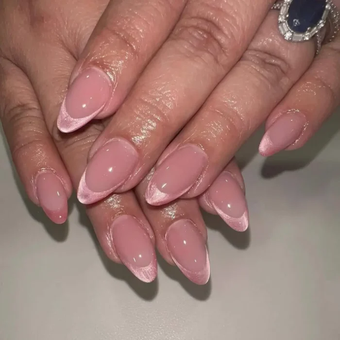 A close-up of an elegant French manicure on almond nails, where the tips are created with a soft pink cat eye polish.
