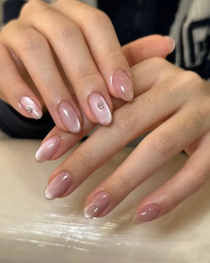 A close-up of a sophisticated pink cat eye manicure on oval nails, with a single rhinestone accent on some nails.