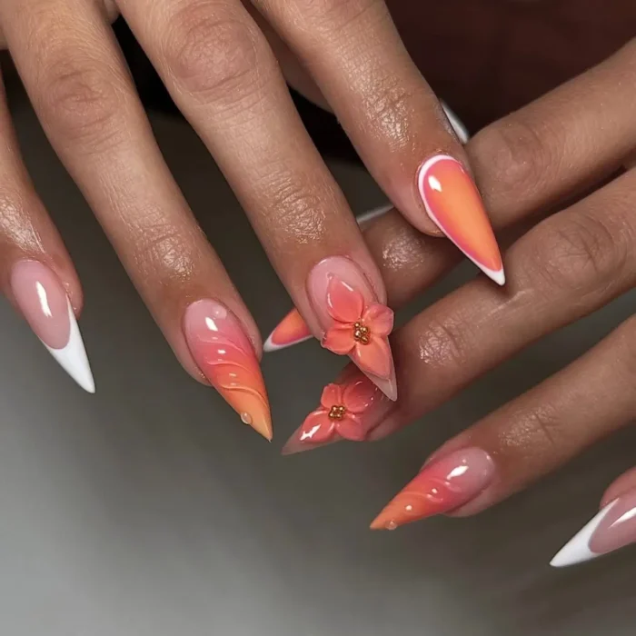 Long stiletto nails with coral and orange ombre, sculpted textures, 3D coral flowers, and white French tips.