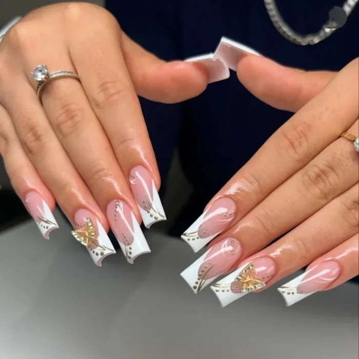 Elegant white nail design on long square nails, featuring a deep French tip, gold butterfly charms, and delicate swirl details.