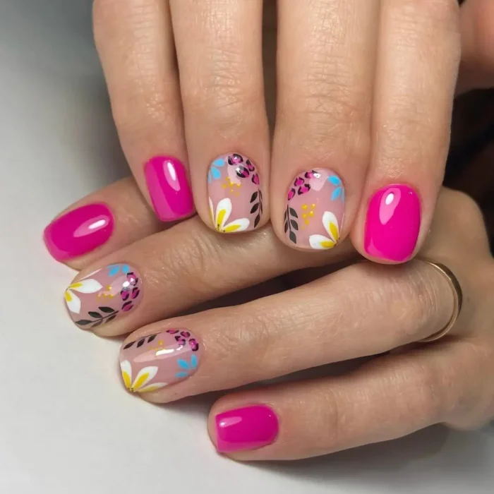 Short, oval nails with a mix of solid hot pink gel polish and sheer nude nails featuring abstract floral designs in white, yellow, blue, and black, with leopard print accents.