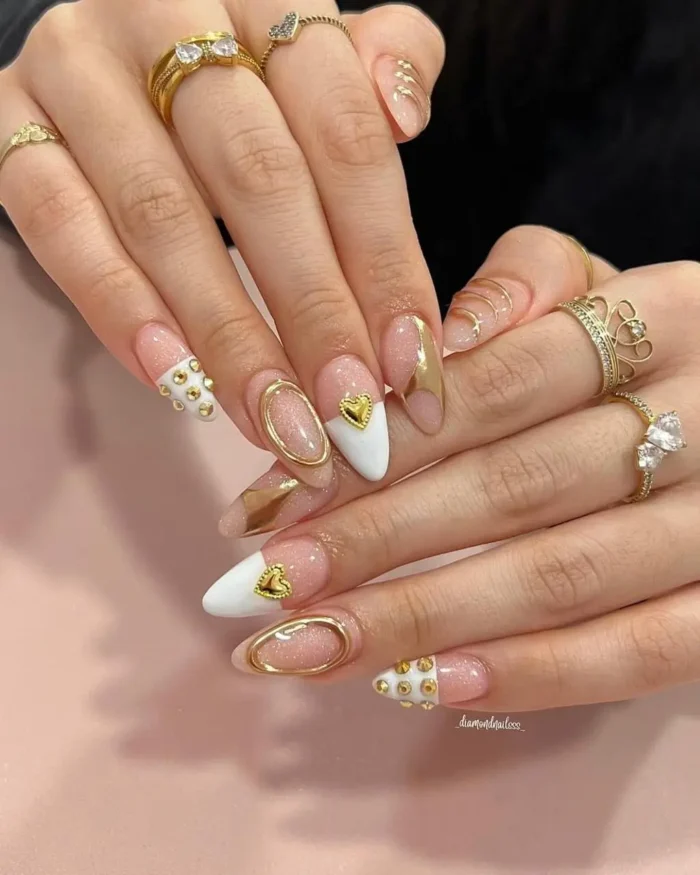 Elegant white nail design on almond nails with mixed media gold accents, including 3D heart charms, gold frames, and beads.