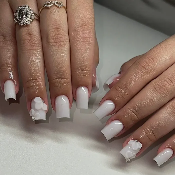 A simple white nail design on square nails with a milky finish, featuring textural 3D white floral accents.