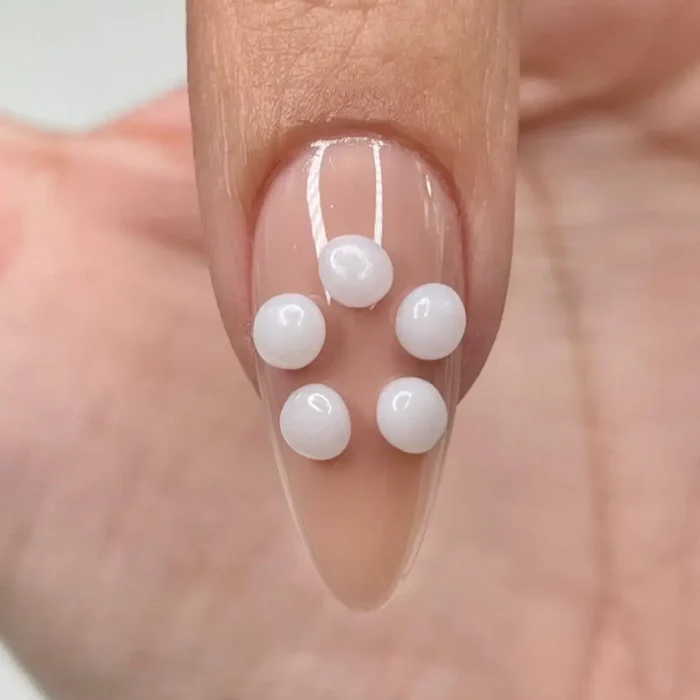 A close-up of a manicured nail with five small white beads of sculpting gel placed in a flower pattern.