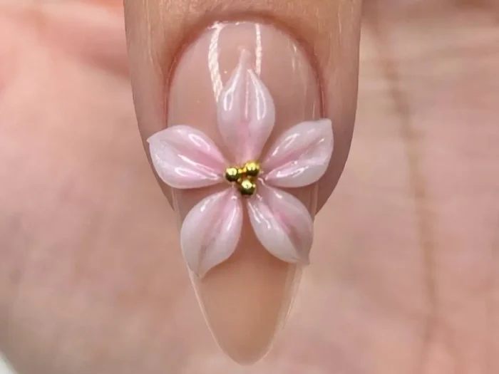 A stunning close-up of a finished look from a 3d flower nail art tutorial, showing a delicate pink and white sculpted flower with a gold bead center on a chic almond-shaped nail.