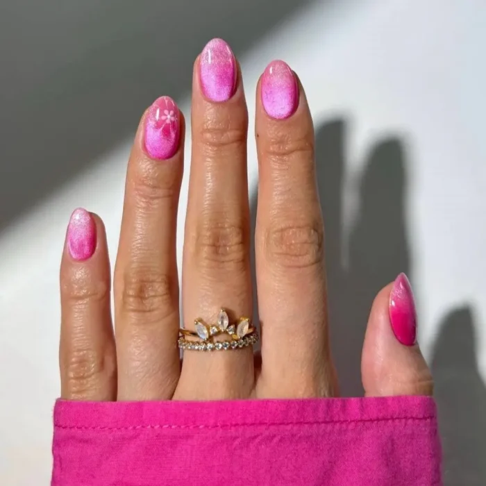 A vibrant pink cat eye manicure on oval nails with a delicate white floral sparkle accent nail.