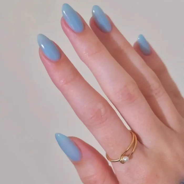 A hand with glossy, almond-shaped nails painted in a serene, dusty cornflower blue.