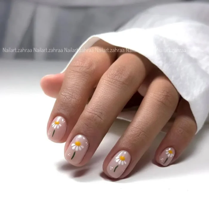 Short nails painted with a sheer pink base and delicate white daisy designs with yellow centers, accented by small white dots.
