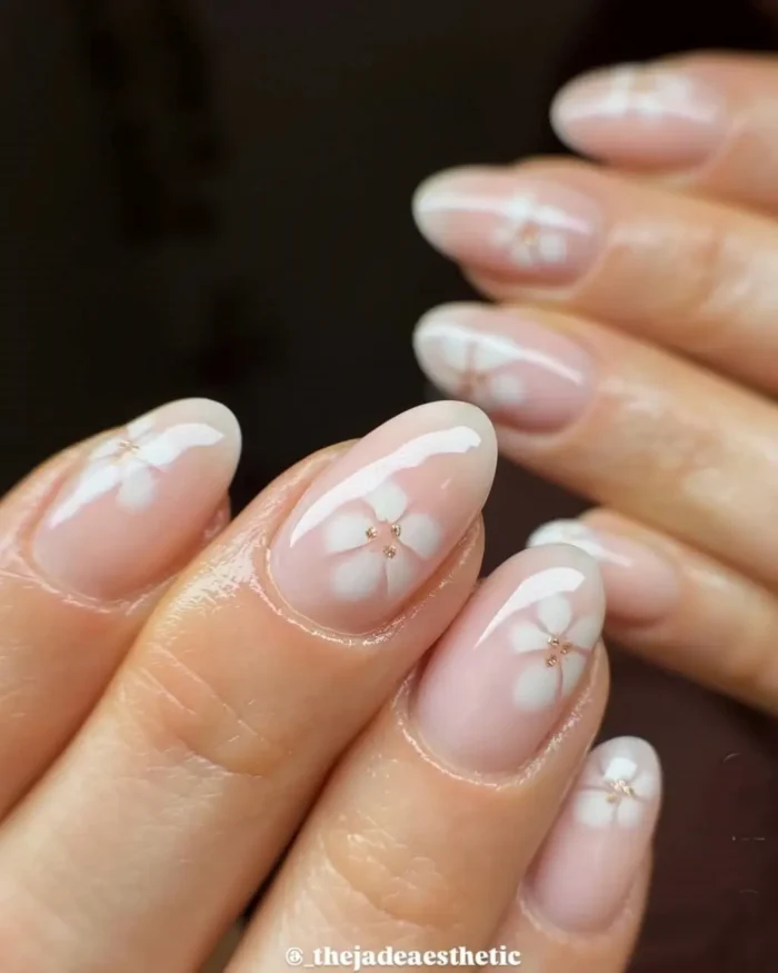 A simple white nail design on short rounded nails, with blooming translucent white flowers and gold bead centers.