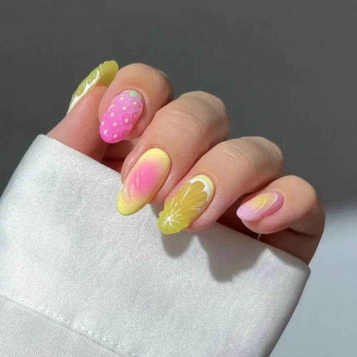 Close-up of a vibrant fruit nail design with a pink and yellow aura gradient, detailed with strawberry and lemon slice art.