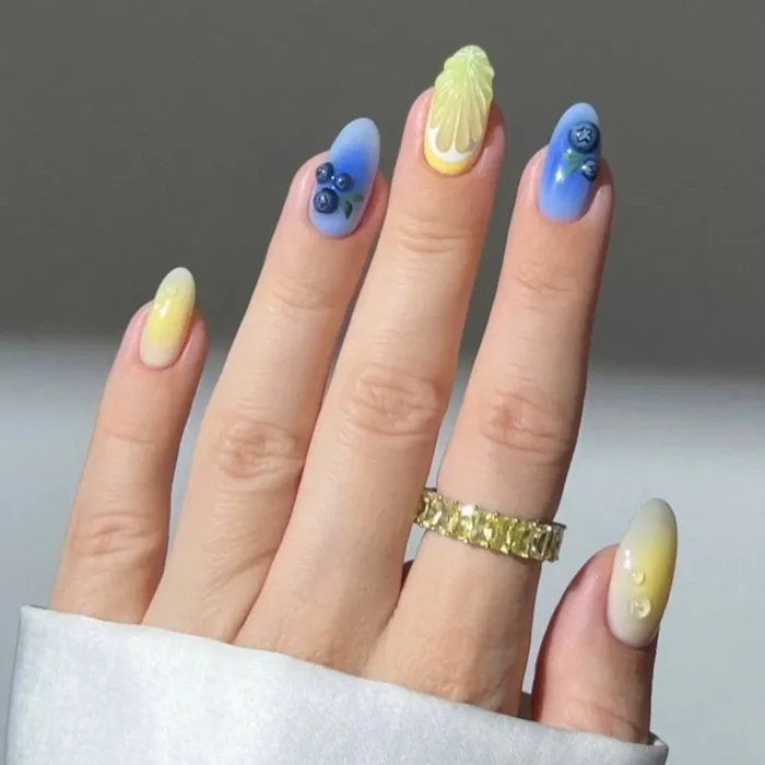 A chic fruit nail design on almond nails, showing a blue and yellow gradient with blueberry art and a 3D lemon slice.