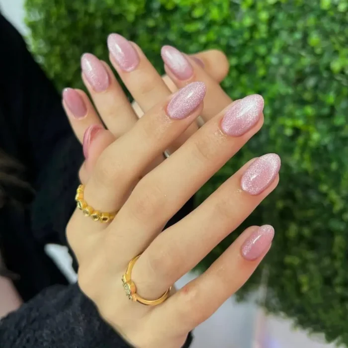 Hands with a sparkling diamond-dust pink cat eye manicure on medium almond-shaped nails.
