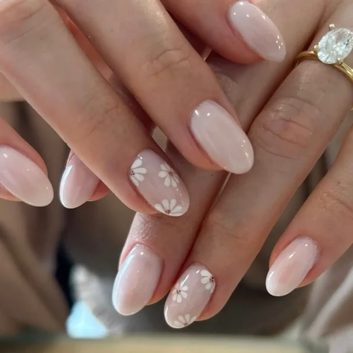 A simple white nail design on short oval nails, with a milky sheer base and cute white daisy accent nails.