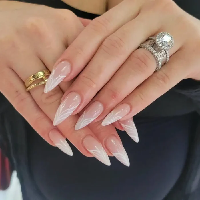 An elegant white nail design on stiletto nails, featuring abstract, leaf-like white patterns at the tips.