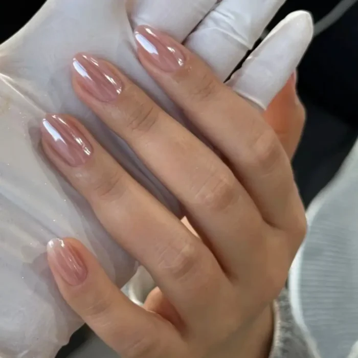 Short, oval-shaped nails with a glossy, sheer, pearlescent nude gel polish, creating a glazed finish.