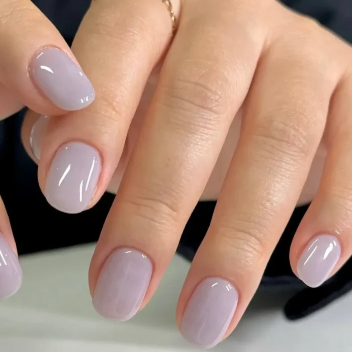 A beautiful close-up of a glossy, hazy lavender-gray manicure on perfectly shaped short, round nails.