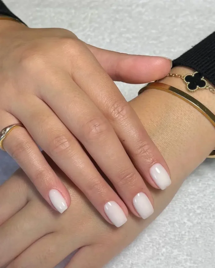 A simple white nail design on short squoval nails featuring a clean and elegant milky finish.