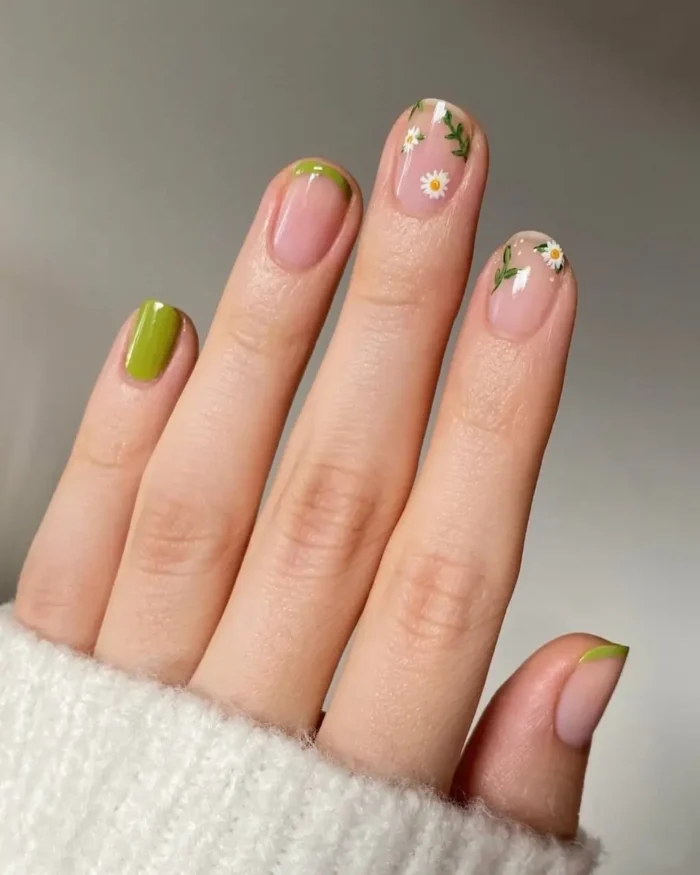 Short nails with a nude base, featuring vibrant green French tips and intricate white daisy and green leaf designs on accent nails.