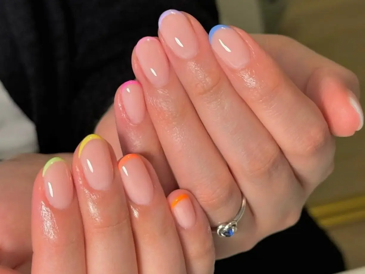 Close-up of short, oval-shaped nails with clear gel base and vibrant rainbow French tips, ideal for a chic short gel manicure thumbnail.