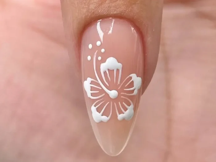 A close-up of a completed white hibiscus flower nail art design on a sheer neutral base, showing the final result of the DIY tutorial.