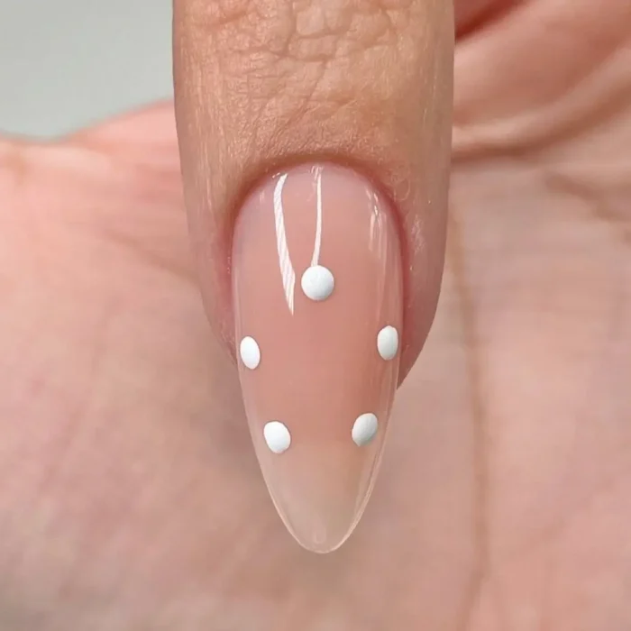The first step of a hibiscus nail tutorial, showing five white dots placed in a circle on a sheer neutral base to map out the flower.