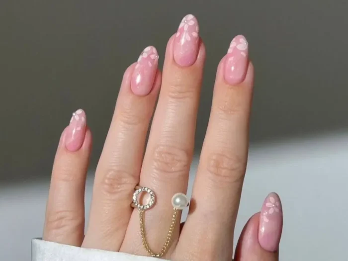 A hand with oval-shaped pretty pink nails featuring delicate white watercolour blossom art.