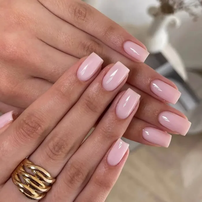 A close-up of a simple pink nail design featuring perfectly manicured square-shaped nails coated in a glossy, milky light pink polish.
