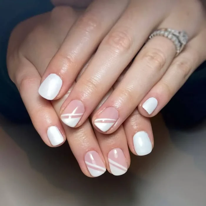 A close-up of a manicure with a simple white nail design, featuring minimalist diagonal white stripes on accent nails.