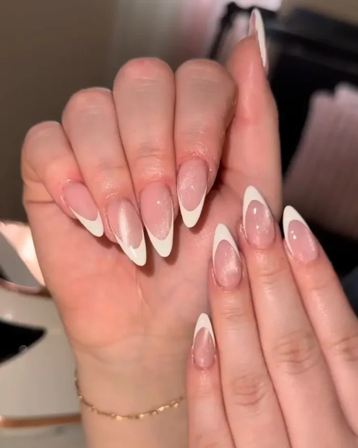 A close-up of almond nails with a classic white french tip over a shimmering cat eye base.