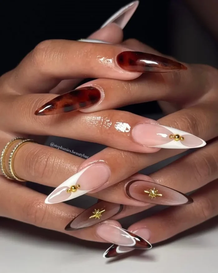 Long stiletto nails with some featuring tortoiseshell patterns and others with white French tips accented by gold studs and star charms.