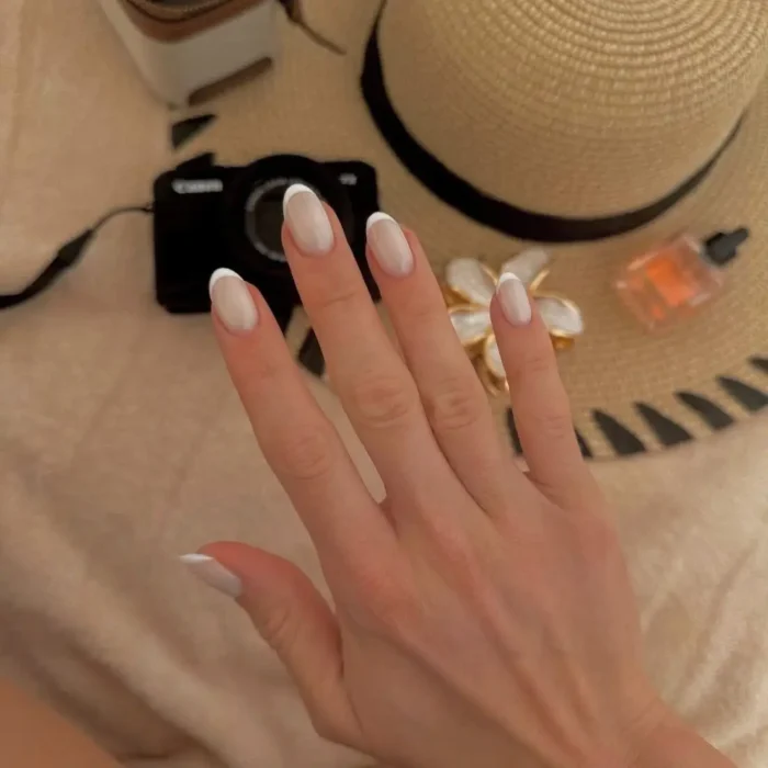 A simple white nail design showing a classic French manicure on short, natural-looking nails.