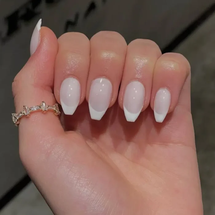 A hand showing a classic soft French manicure on short, neatly shaped nails with a milky base.
