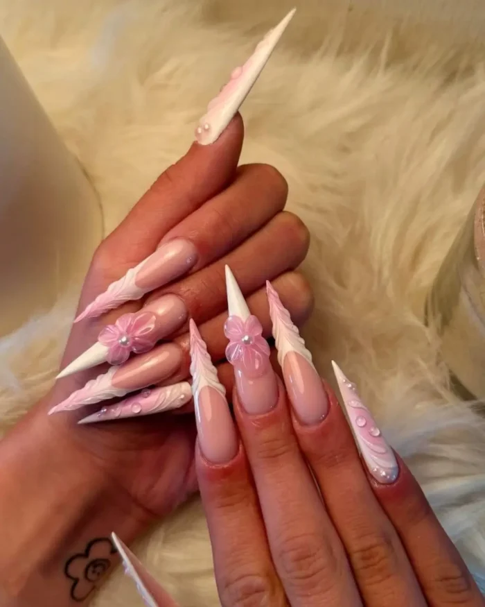 Extremely long stiletto nails with sculpted white tips, 3D pink flowers, and pearl details.