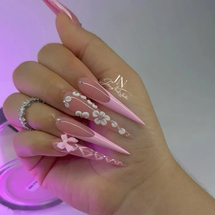 A romantic pink stiletto nail design with a 3D bow and cascading white flowers.