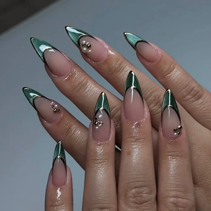 A detailed view of long stiletto nails with a green cat eye french tip, black outline, and pearl accents.
