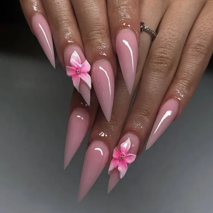 Long, glossy baby pink stiletto nails with delicate 3D pink and white flowers on accent nails.