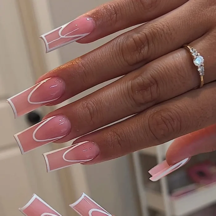 A close-up of a hand with long, square-shaped nails featuring a graphic white abstract line design on a pink base.