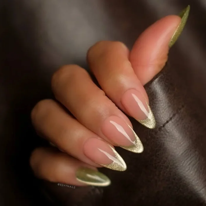 A close-up of almond nails with a gold glitter french tip and an olive green cat eye effect.