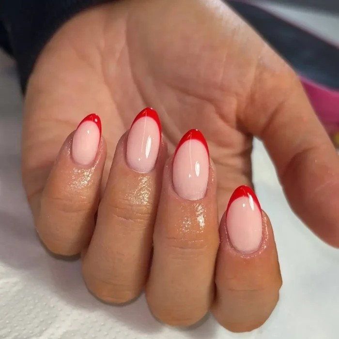 A close-up of a hand showcasing a chic red French manicure on glossy, short oval nails.