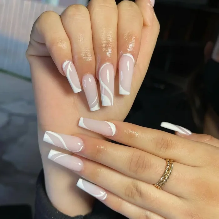 Hands showing long, square nails with a simple white nail art design of bold, graphic swirls.