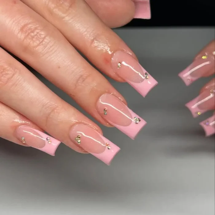 A close-up of a French manicure with long square nails, featuring bright pink tips and small rhinestones scattered along the smile line.