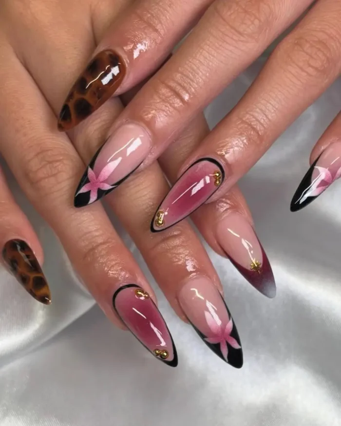 Long stiletto nails with tortoiseshell pattern and black-outlined tips, some with pink and red gradients and star designs with gold studs.