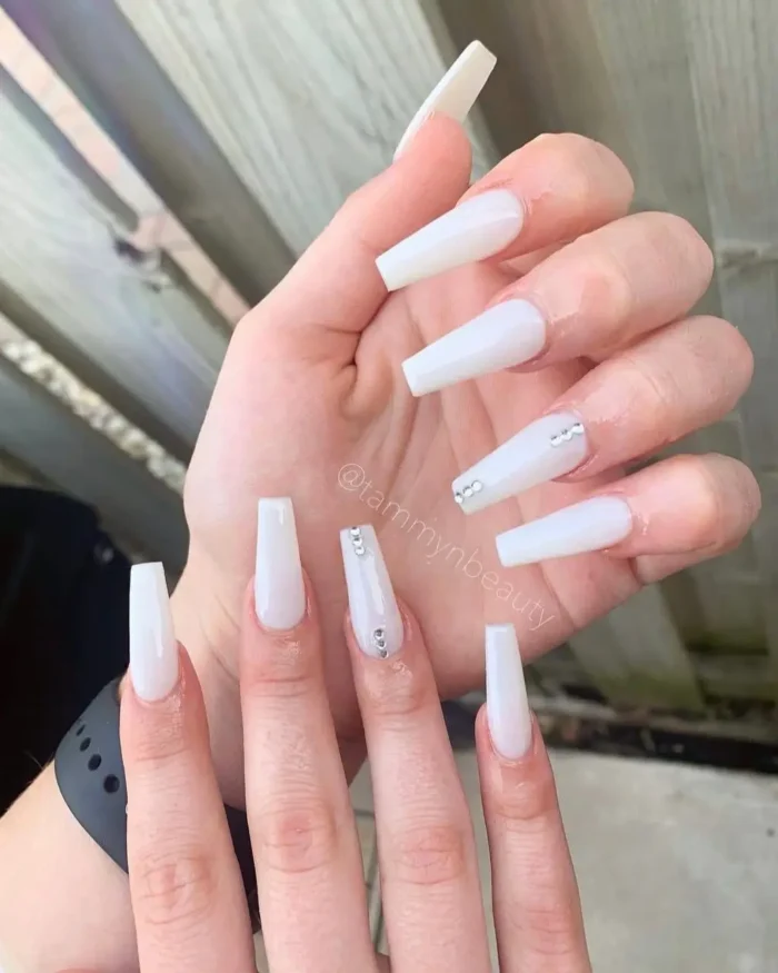 A simple white nail design in a milky shade on long coffin nails, adorned with subtle rhinestone accents.