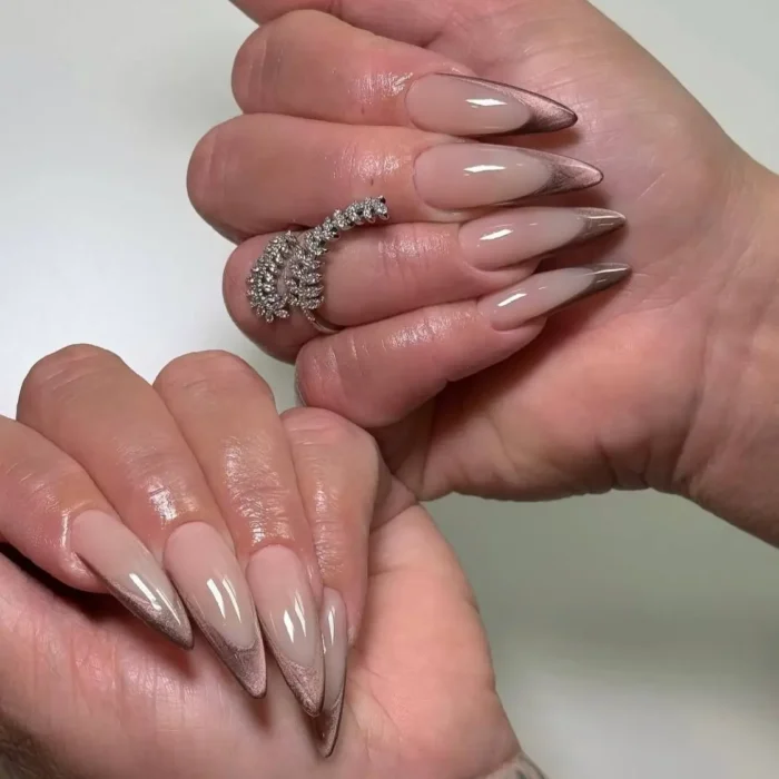 A close-up of long stiletto nails with a sharp rose gold cat eye V-french tip.