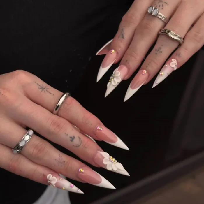 Long stiletto nails with white French tips, decorated with 3D white flowers and small colorful rhinestones.