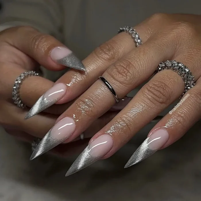 A dramatic close-up of long stiletto nails with a highly reflective silver glitter french tip.