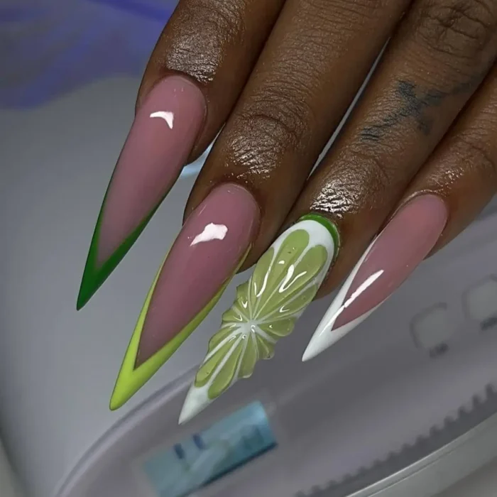 Long stiletto nails with pink bases and green French tips, one accent nail designed as a 3D lime slice.