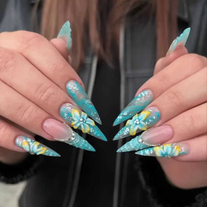 Long stiletto nails with aqua and white marble effect, white speckles, silver lines, and 3D yellow and blue flowers.